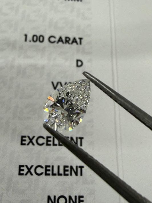 ペアシェイプ 1.00ct DカラーのルースをIGI鑑定書の上でピンセットで持ったところ
